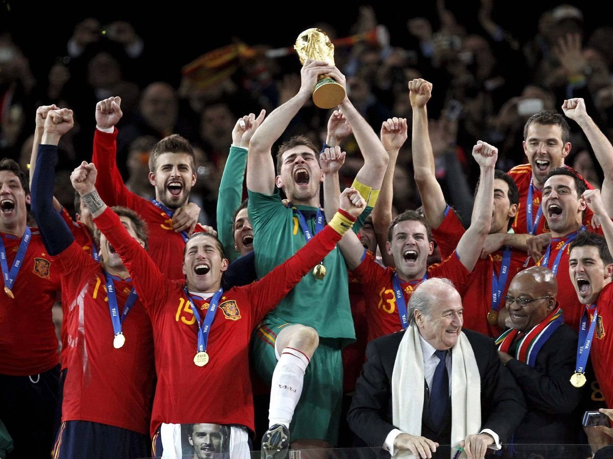 Spanish soccer team celebrates World Cup victory, holding trophy aloft with medals around necks in red uniforms