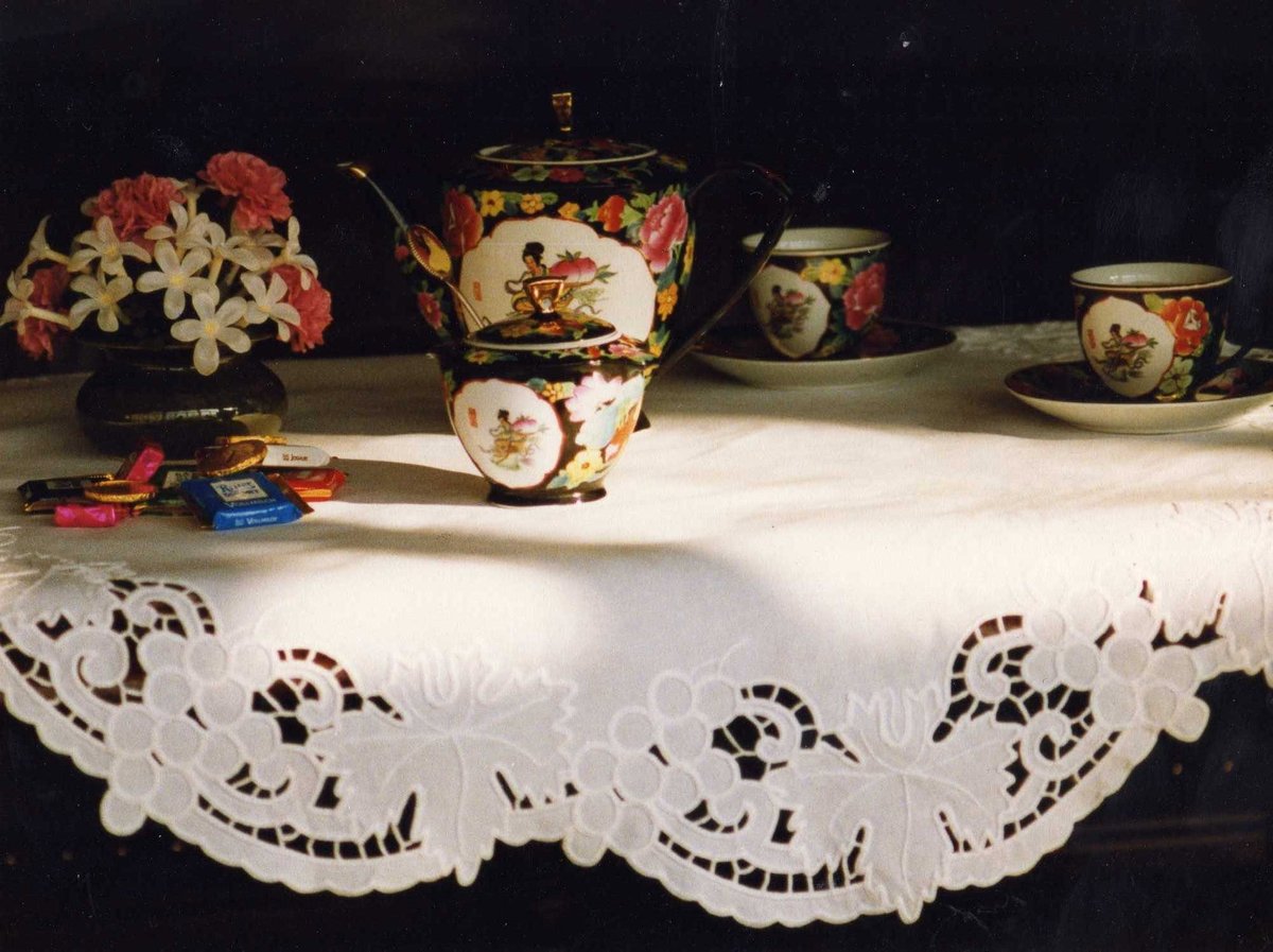 Collection of ornate porcelain teaware with floral patterns displayed on white lace tablecloth against dark background