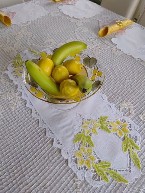Szklana misa z żółtymi cytrynami i zielonymi bananami na bieżniku z żółto-zielonym haftem kwiatowym