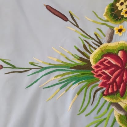 Embroidered floral design featuring red and pink flowers with green spiky petals and yellow accents on white fabric