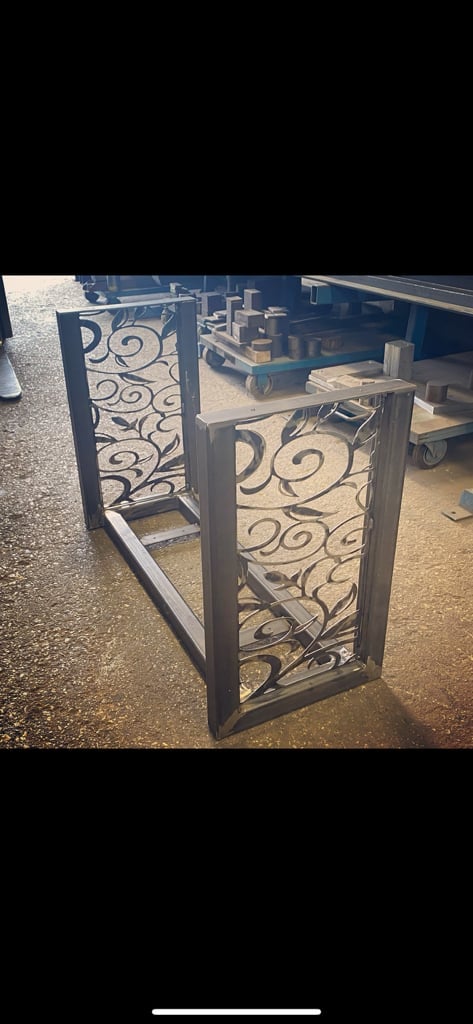 Decorative metal gate panels with scrollwork design and black frame standing in an outdoor workshop area