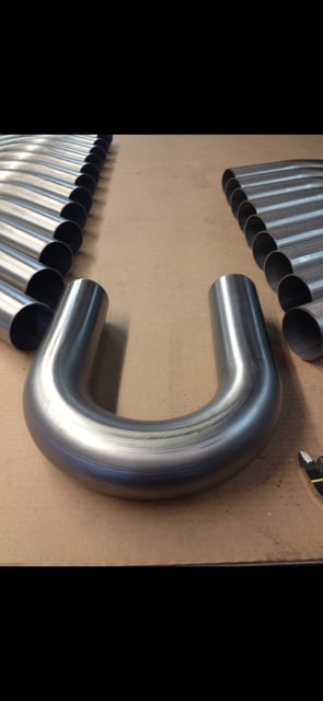 U-shaped stainless steel pipe fitting displayed on beige surface with corrugated metal sections visible