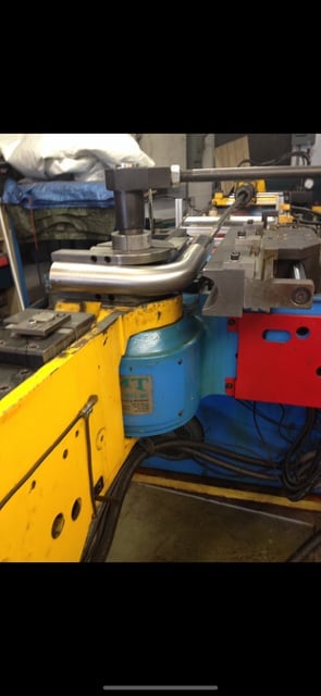 Industrial ductwork fabrication equipment with yellow and blue machinery, metal piping, and tools in a workshop
