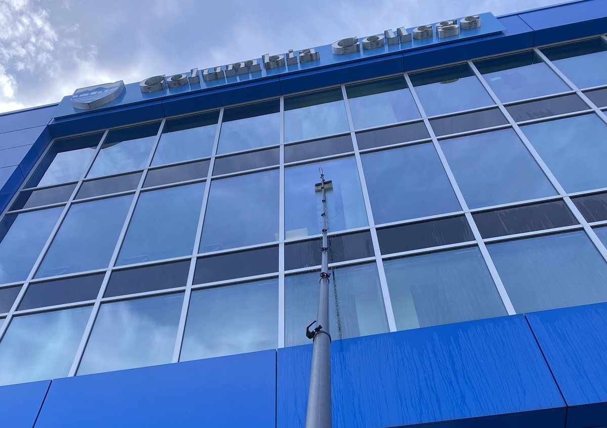 Modern blue building facade with large grid-patterned windows and metal framework against cloudy sky