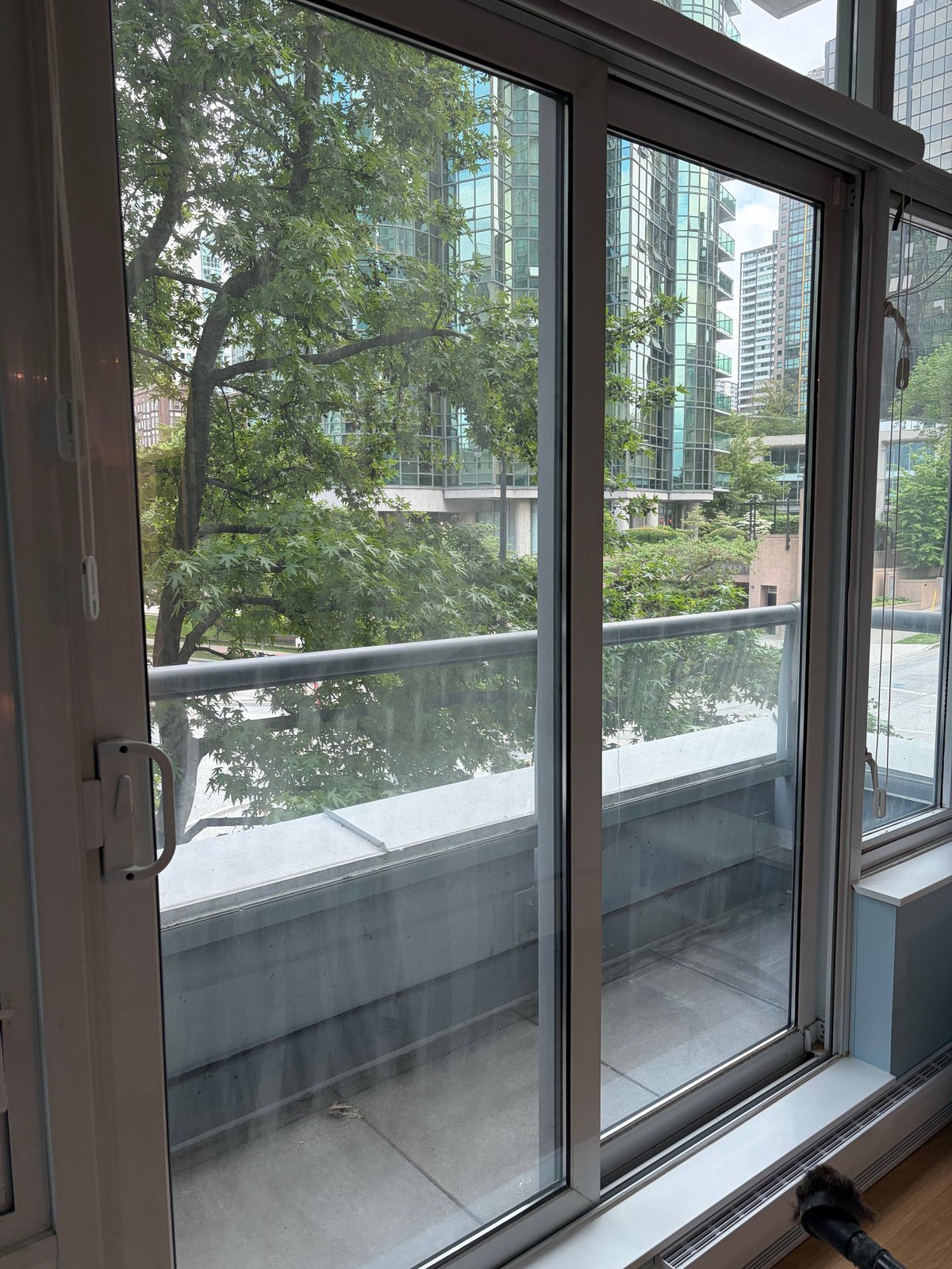 Large glass sliding doors opening onto a balcony overlooking trees and urban skyscrapers