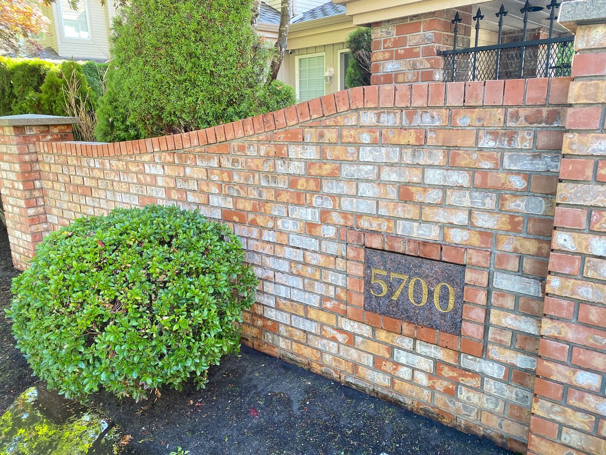 Red brick fence with house number 5700 and green spherical shrubs in landscaped front yard