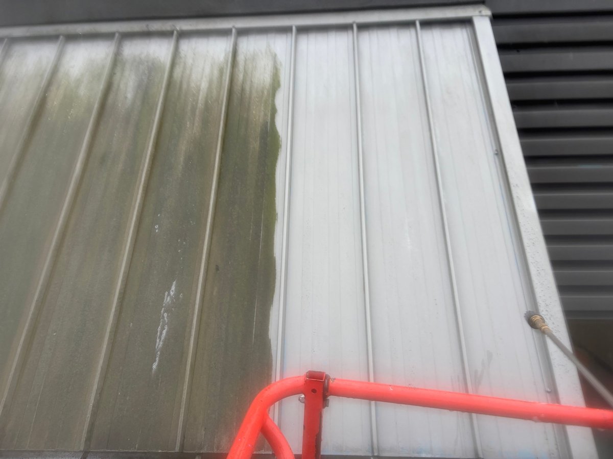 Metal roof with corrugated panels showing algae growth on left side and red metal frame in foreground