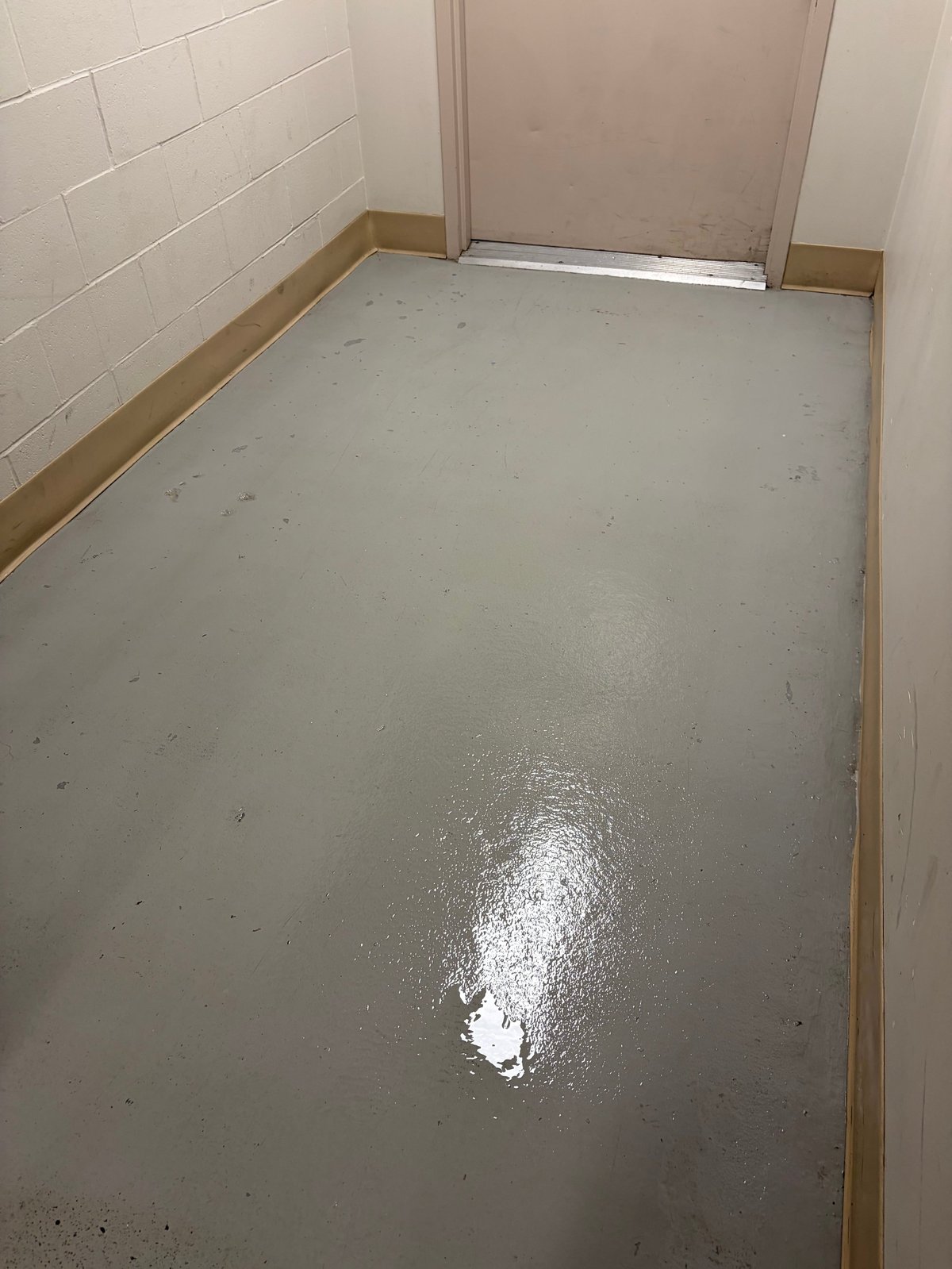 Empty bathroom or utility room with gray concrete floor, white subway tile walls, and partial door visible at back.