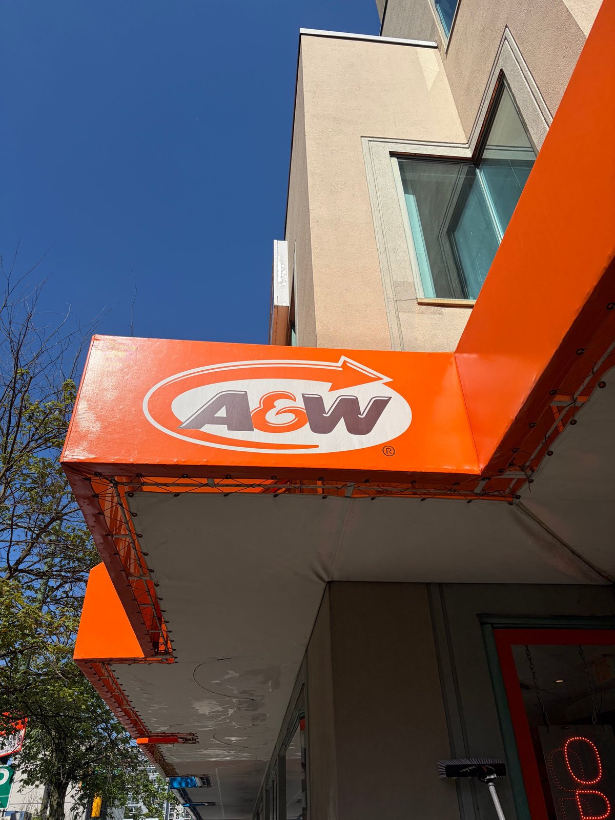 Bright orange A&W restaurant sign mounted on a storefront canopy against a clear blue sky