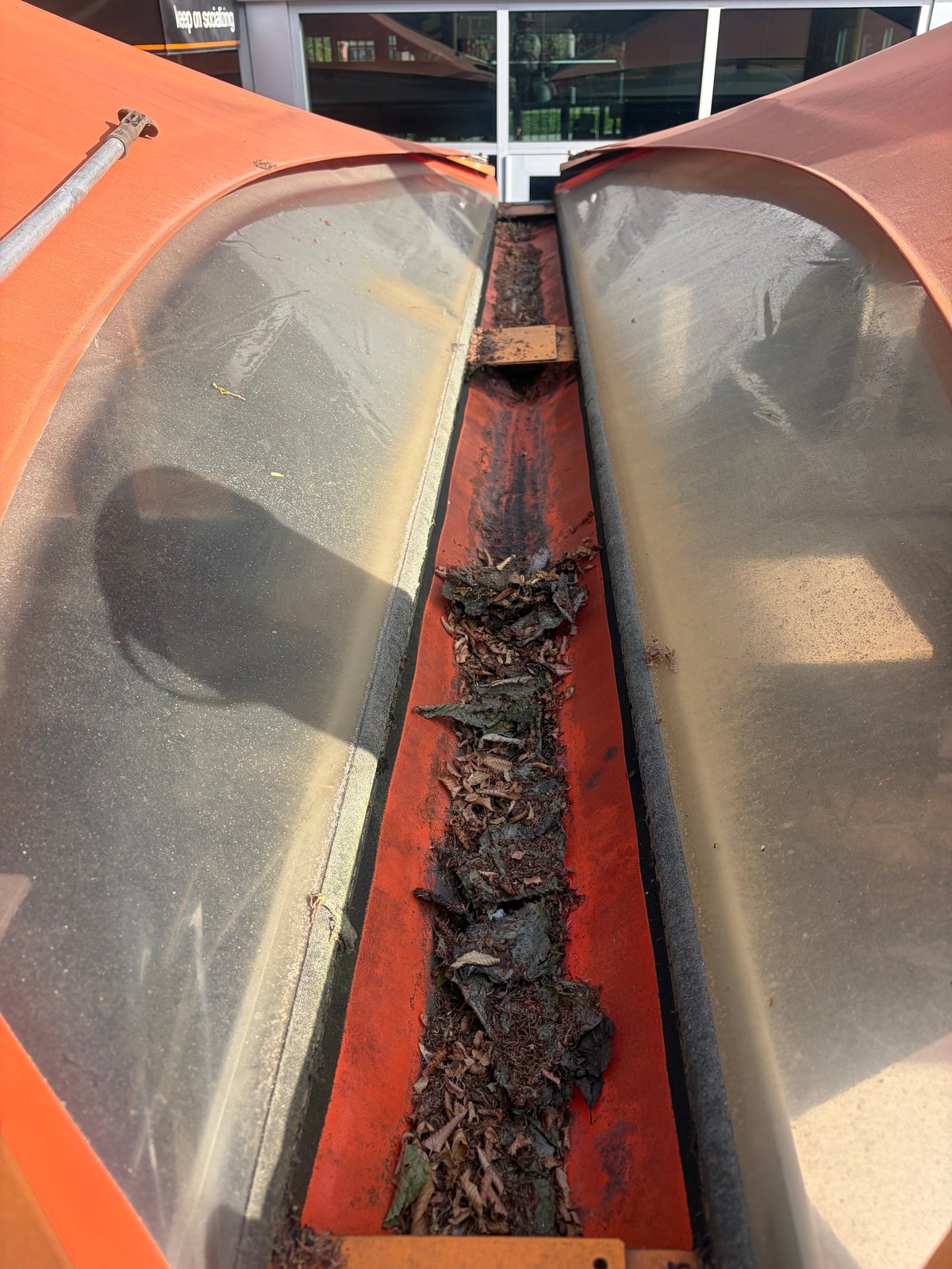 Overhead view of an orange agricultural truck bed with two metal tanks separated by a rust-stained red divider filled with organic debris