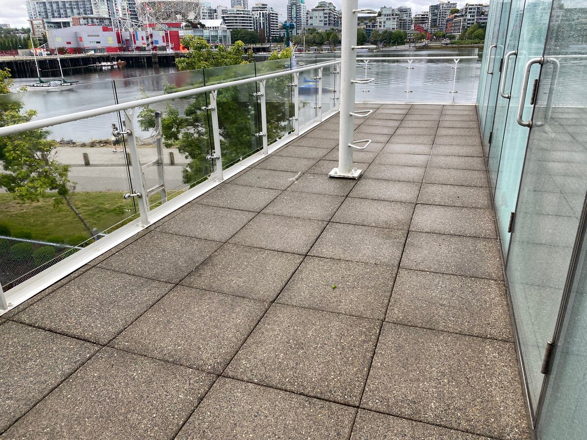 Modern rooftop terrace with gray paved flooring, glass railing, and view of waterfront city skyline with river and buildings