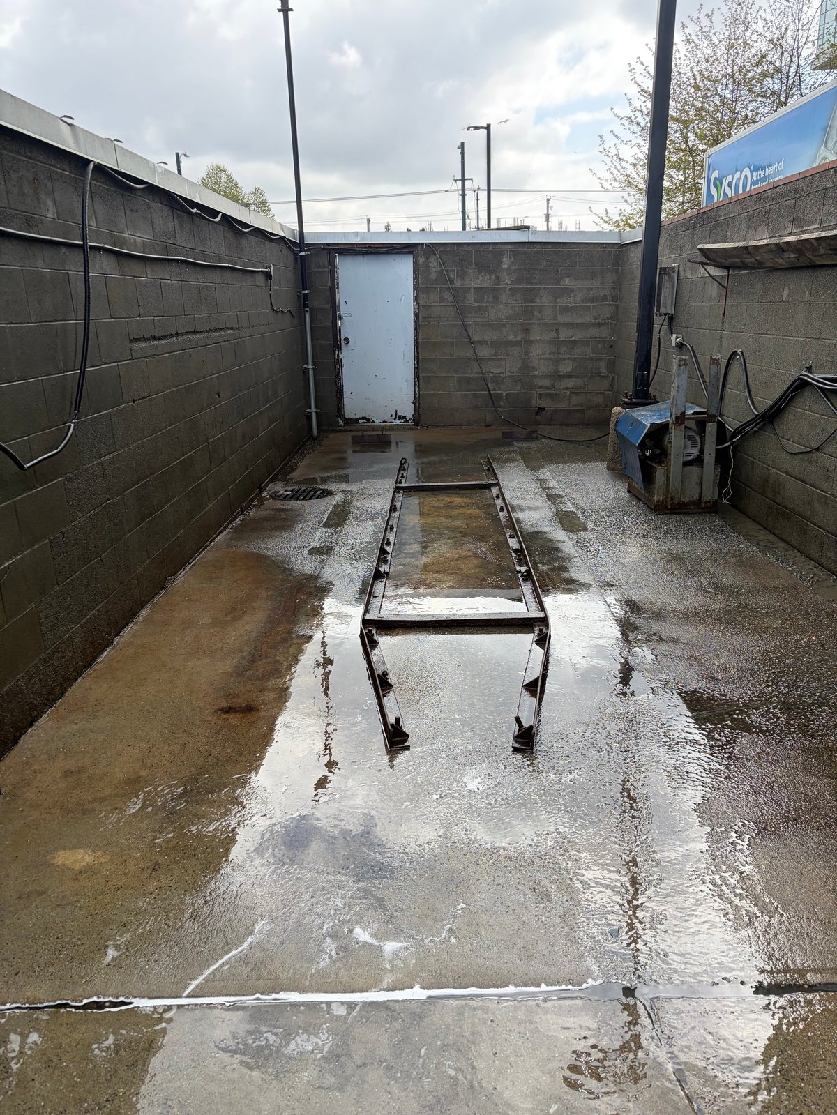 Industrial concrete pit with metal framework and wet flooded floor, featuring walls and utility equipment