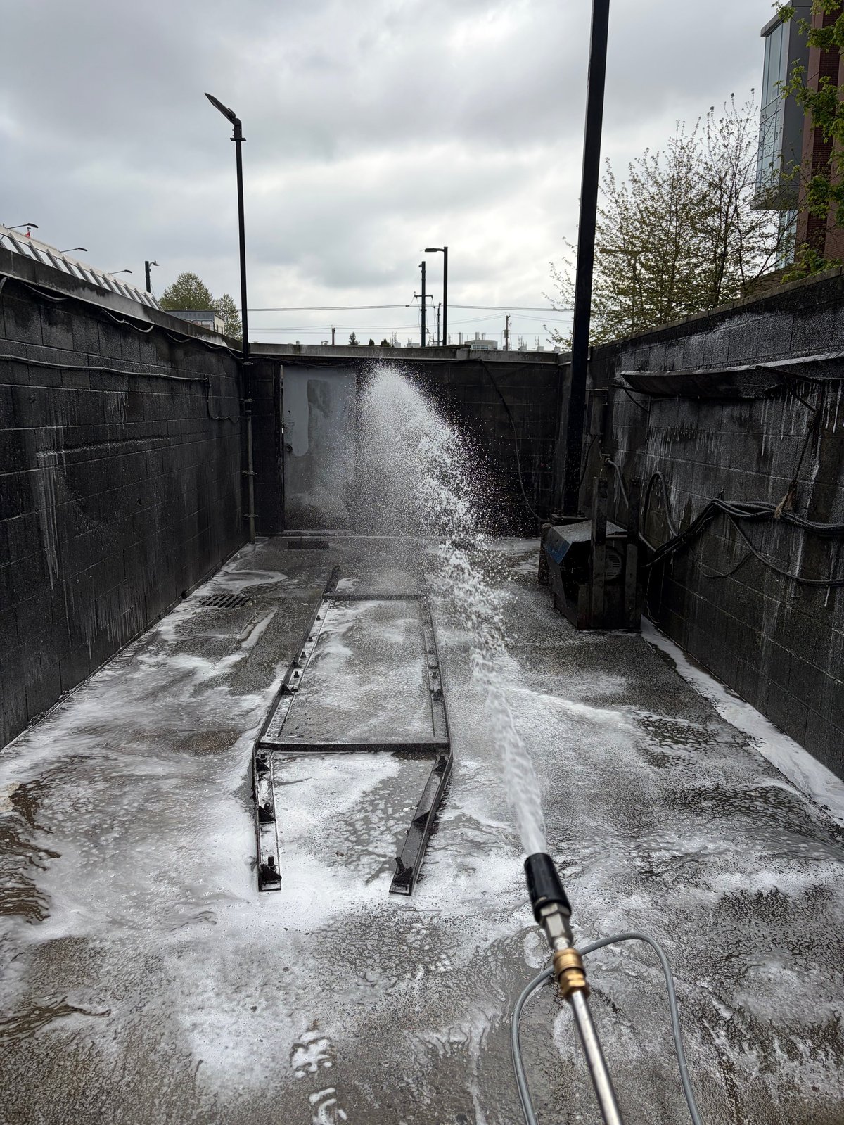 High-pressure water spray cleaning a concrete lock chamber with metal walls under cloudy sky