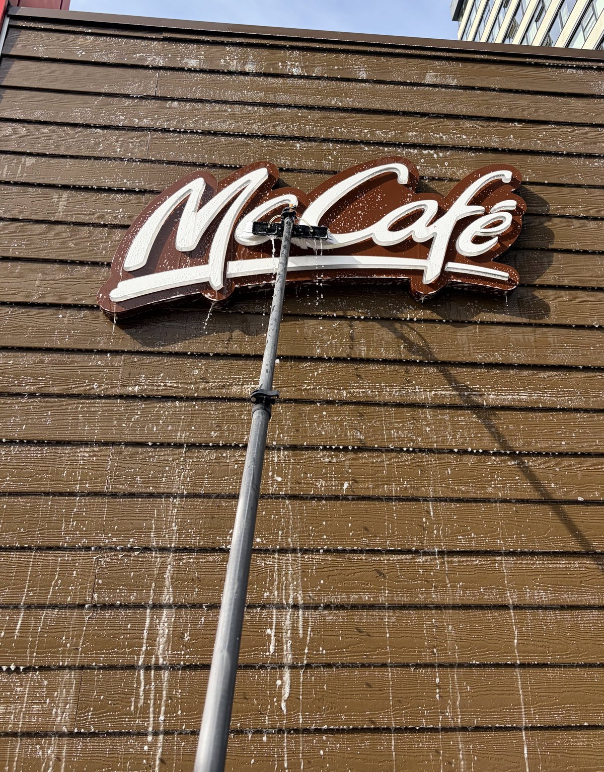 Neon sign reading McCafe mounted on a wooden slatted wall with a metal pole