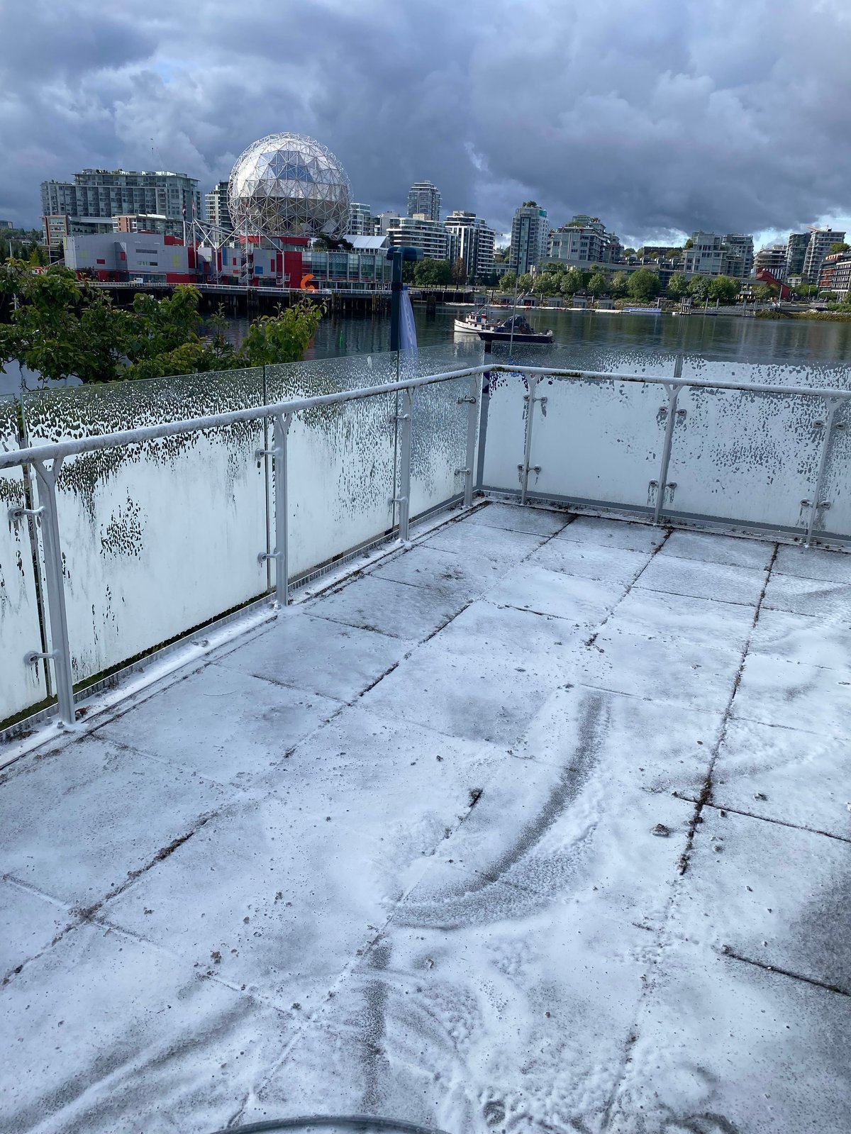 View from a wet rooftop platform overlooking Science World dome, river, and Vancouver cityscape with stormy sky
