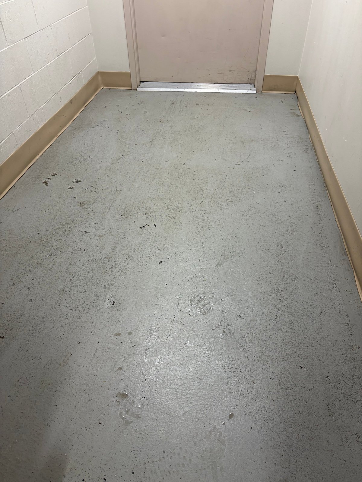 Empty concrete shower floor with white tile walls and chrome door frame at entry