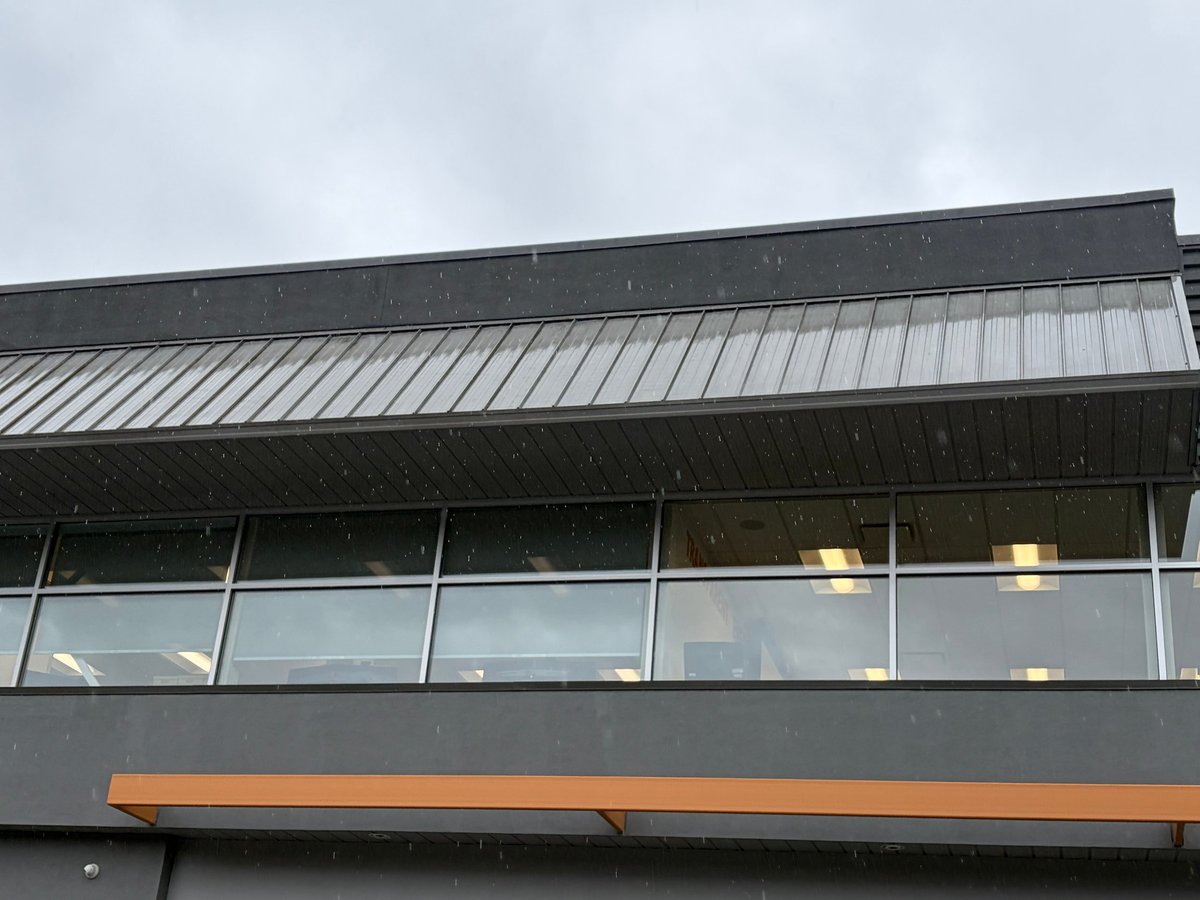 Modern industrial building exterior with metal roof, horizontal windows, and orange trim detail under overcast sky