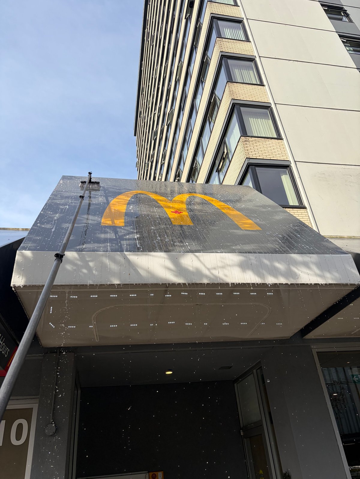 Modern building storefront with yellow curved logo on grey awning and vertical ribbed facade above