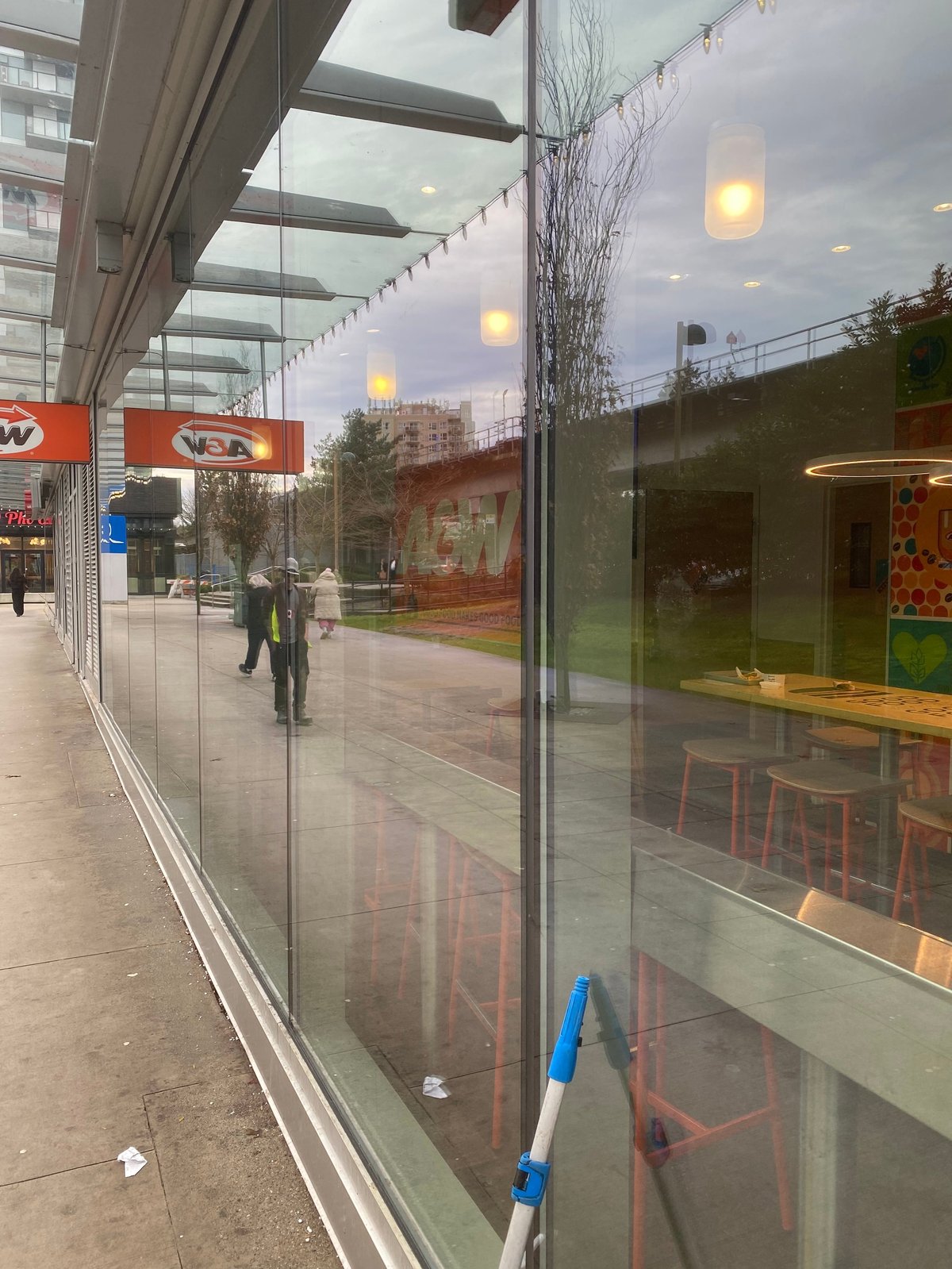 Modern urban storefront with glass windows and doors at dusk, showing city street view with buildings and string lights