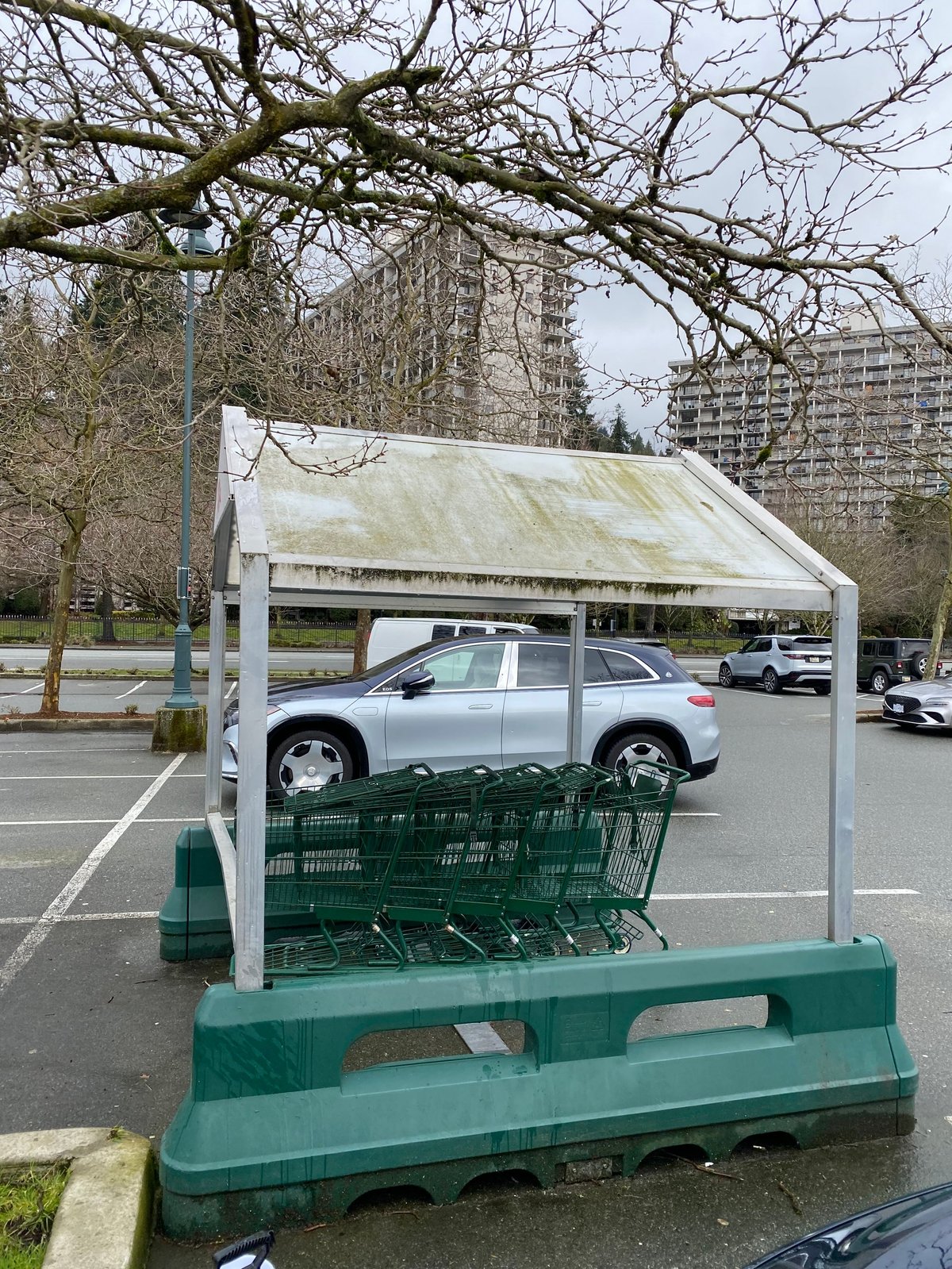 White canopy structure with stacked green plastic crates in a parking lot, with a silver SUV and residential buildings in the background