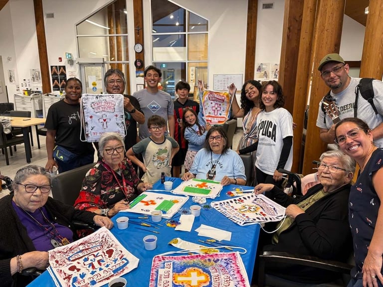 Group of people of various ages gathered around a table with colorful artwork and crafts displayed on a blue surface