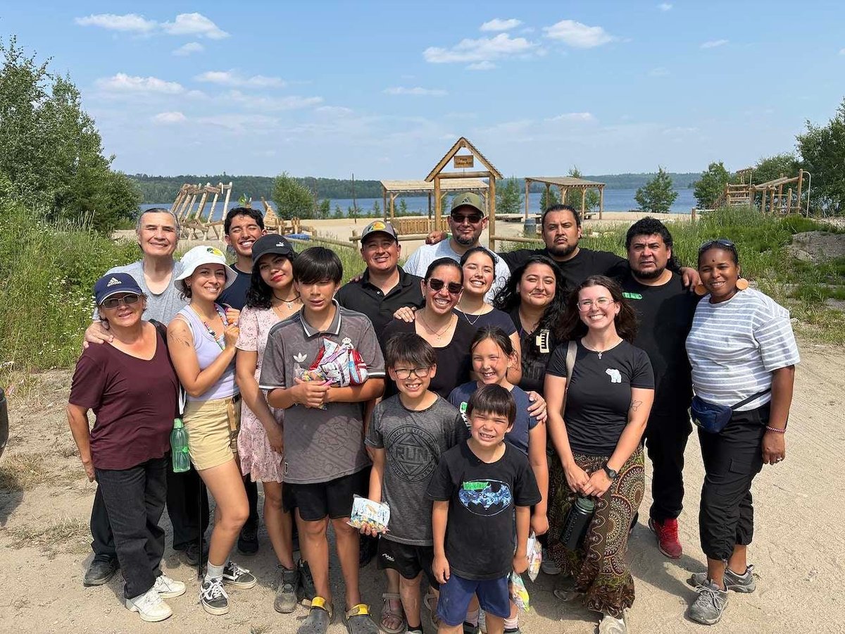 Large group of adults and children posing together at a farm with garden structures and fields visible in the background
