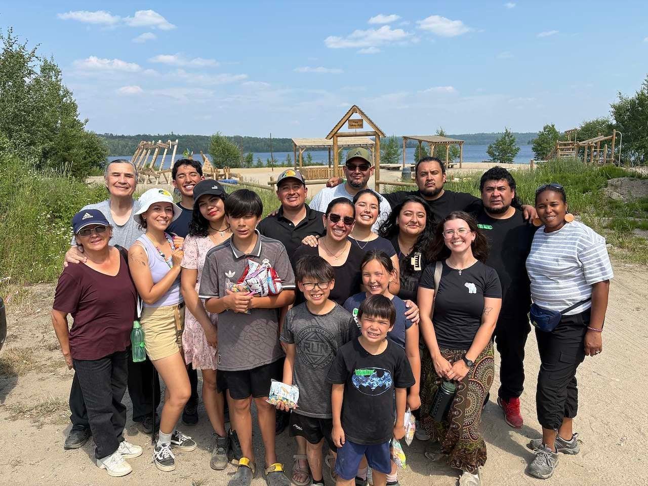 Large group of adults and children posing together at a farm with garden structures and fields visible in the background
