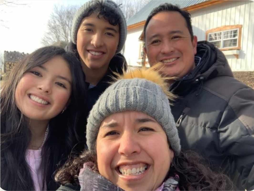 Four people smiling at the camera outdoors in front of a wooden building during winter