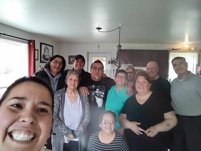 Group of people smiling at the camera during a family gathering in a living room, with one person taking a selfie