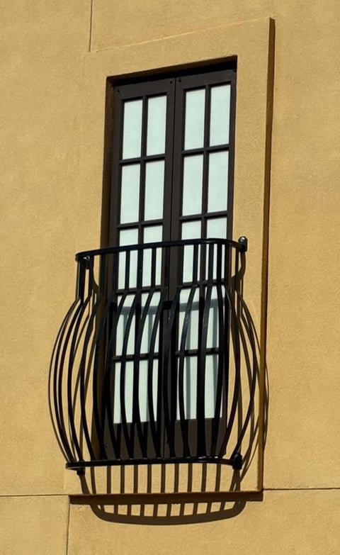 Black wrought iron balcony railing on yellow stucco wall with black-framed window panes