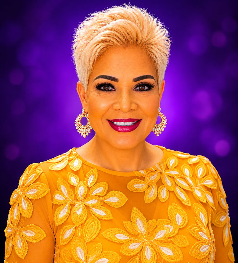 Woman with platinum blonde short hair wearing a yellow floral embellished top and hoop earrings, smiling against a purple bokeh background