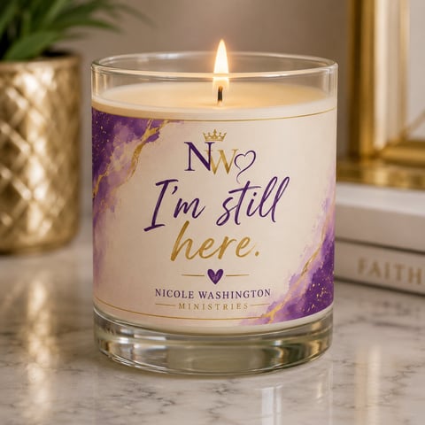 Lit scented candle with Im still here label by Nicole Washington Ministries on marble surface with gold accents