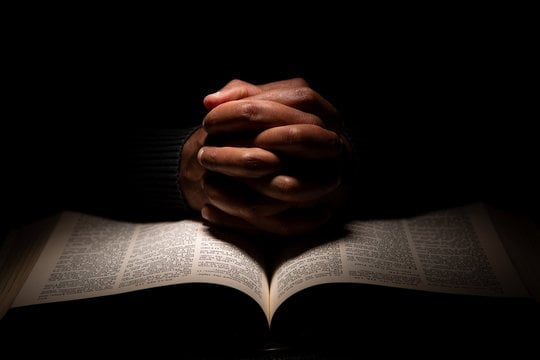 Hands clasped over an open Bible in study and prayer