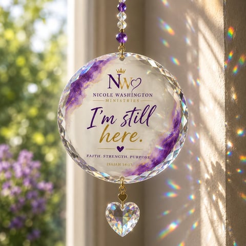 Crystal sun catcher hanging in window with purple floral design, text Im still here, and heart pendant creating rainbow light reflections
