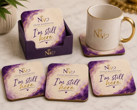 Purple and cream branded coasters and mug with Im still here text, displayed with purple holder on marble surface