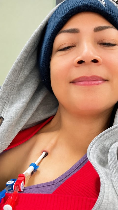 Woman wearing blue beanie and gray hoodie with eyes closed, smiling peacefully