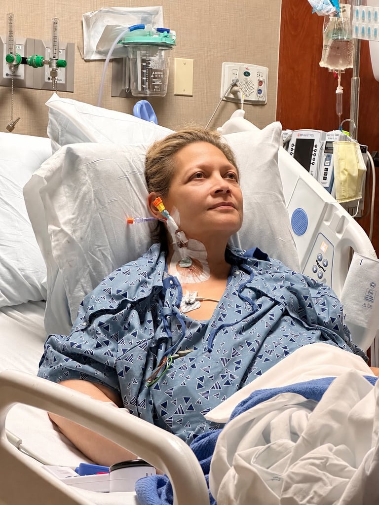 Young patient lying in hospital bed wearing blue patterned gown with medical monitoring equipment visible in background