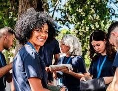 Woman with afro hair smiling while holding a plate at outdoor gathering with diverse group of people