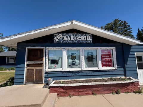 Blue exterior of Ino Bar and Grill restaurant with white-trimmed windows and brick foundation under clear sky