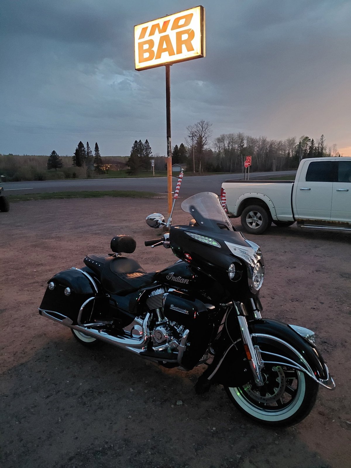Black motorcycle with sidecar parked under an illuminated inn bar sign at dusk in a parking lot