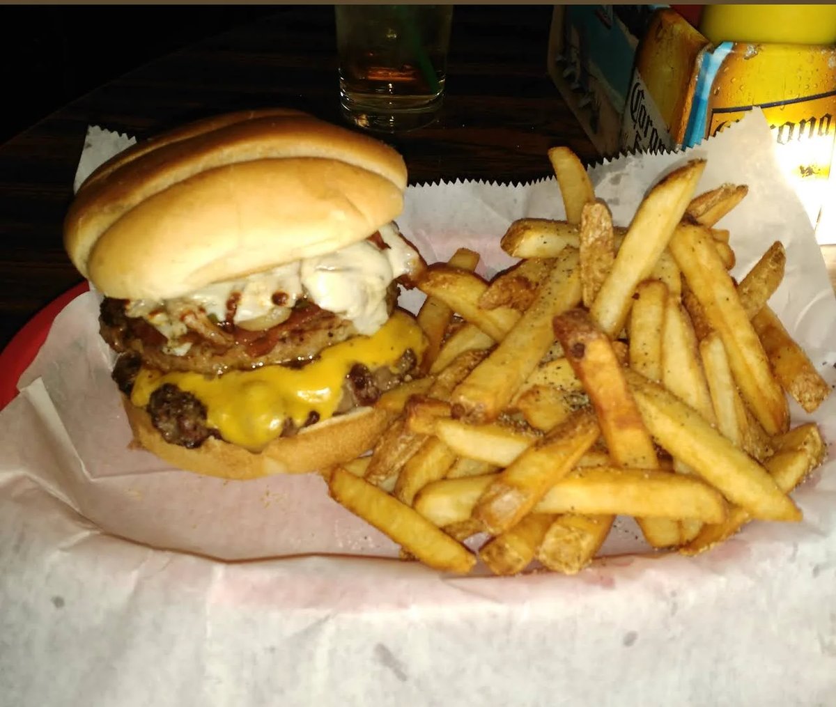 A cheeseburger with caramelized onions and crispy fries on parchment paper with a drink in the background