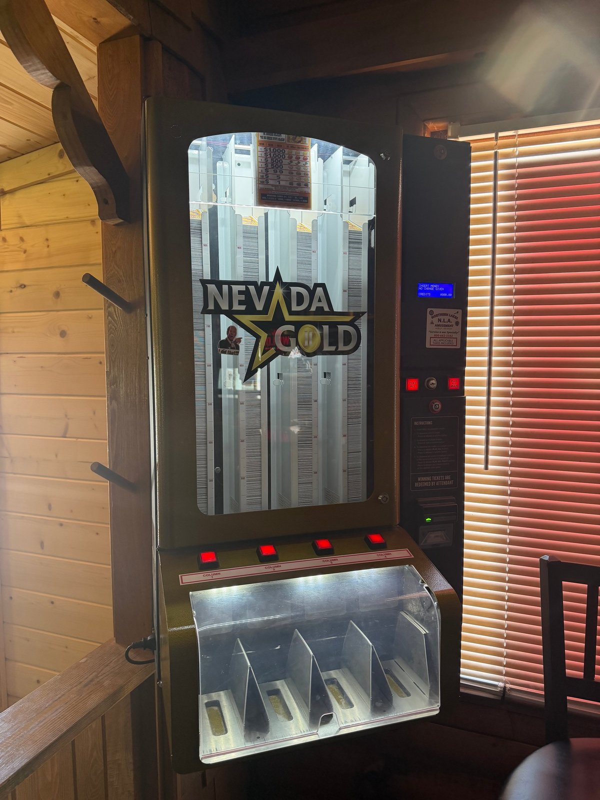 Nevada Gold cigarette vending machine with black exterior, illuminated display, and red control buttons in a wooden interior setting