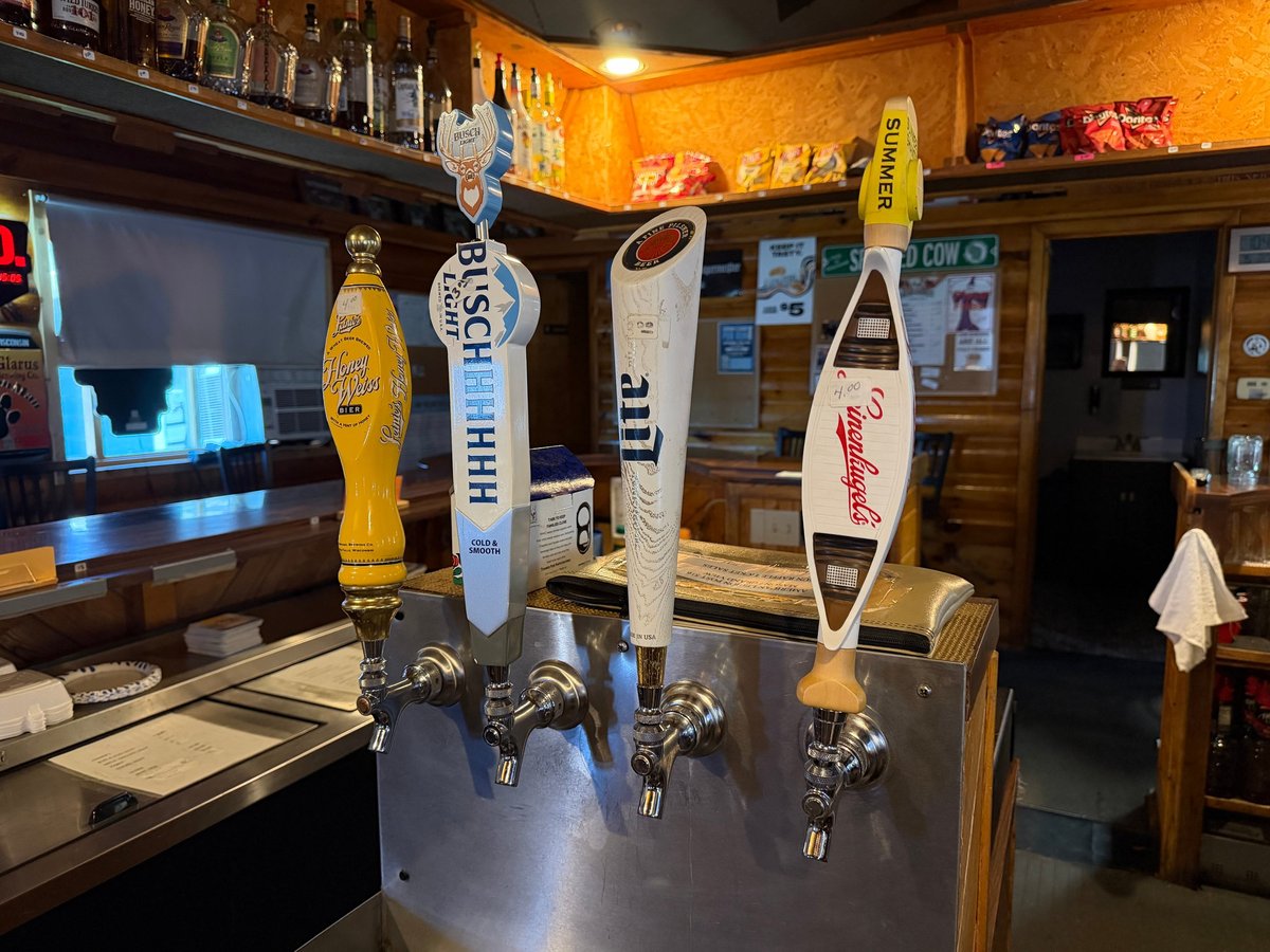 Four beer tap handles with colorful markers mounted on a bar counter in a sports-themed pub with yellow walls and memorabilia.