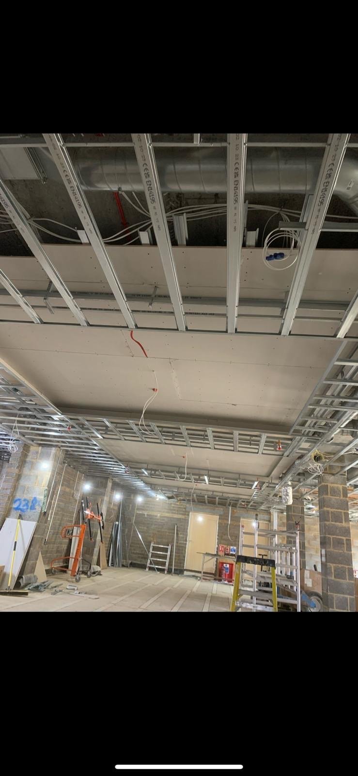 MF ceiling framework with ducting and cabling, ladders and site equipment visible, commercial fit-out.