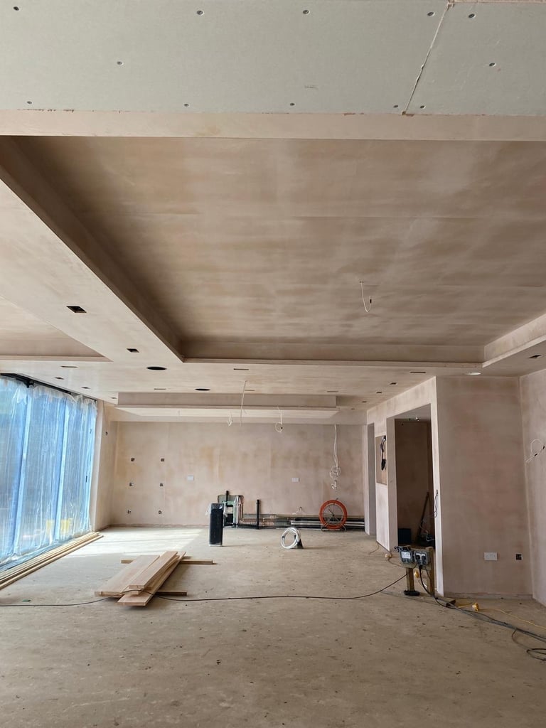 Interior of unfinished room under construction with drywall-covered walls and ceiling, recessed lighting fixtures, and construction equipment
