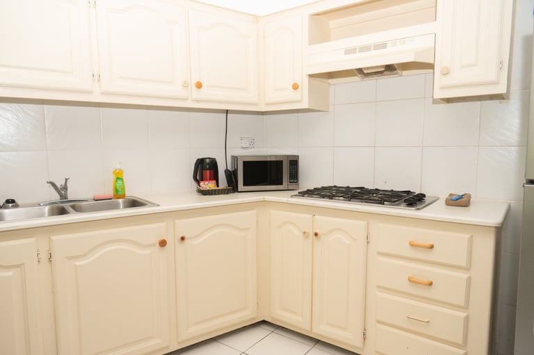 Small kitchen with cream-colored cabinets, white tiled backsplash, gas cooktop, microwave, and sink in corner layout
