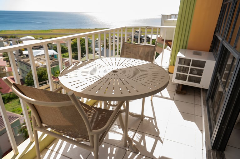 Oceanview balcony with round table, chair, and sunshade overlooking the Caribbean Sea and hillside