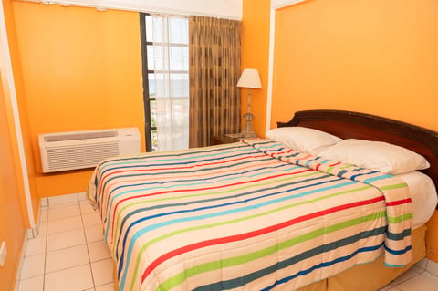 Bright orange bedroom with a colorful striped bedcover on a wooden bed, window with curtains