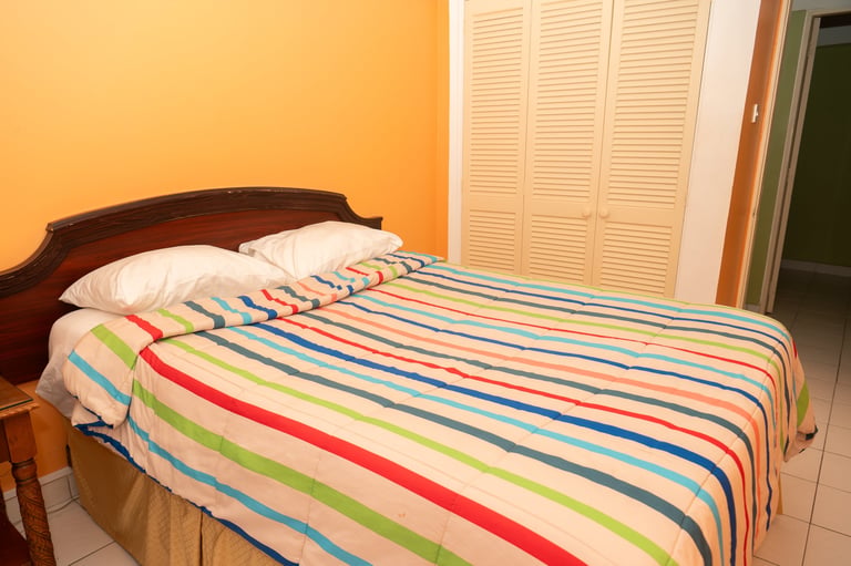 Bedroom with wooden bed featuring colorful striped bedding, orange walls, white closet doors, and white pillows