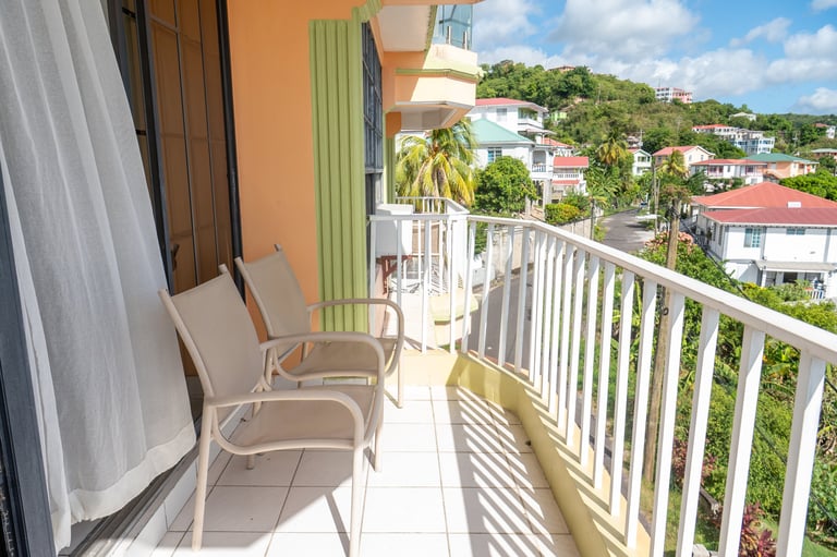Sunny balcony with white railing, beige chairs, and colorful hillside neighborhood